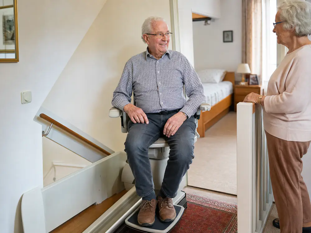 Man komt boven aan met zijn traplift, zijn vrouw begroet hem