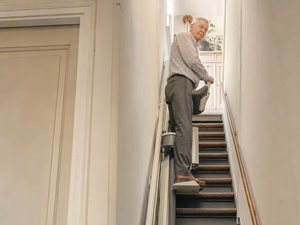 Sta-traplift op een smalle, steile trap, gebruiker leunt op het zitje